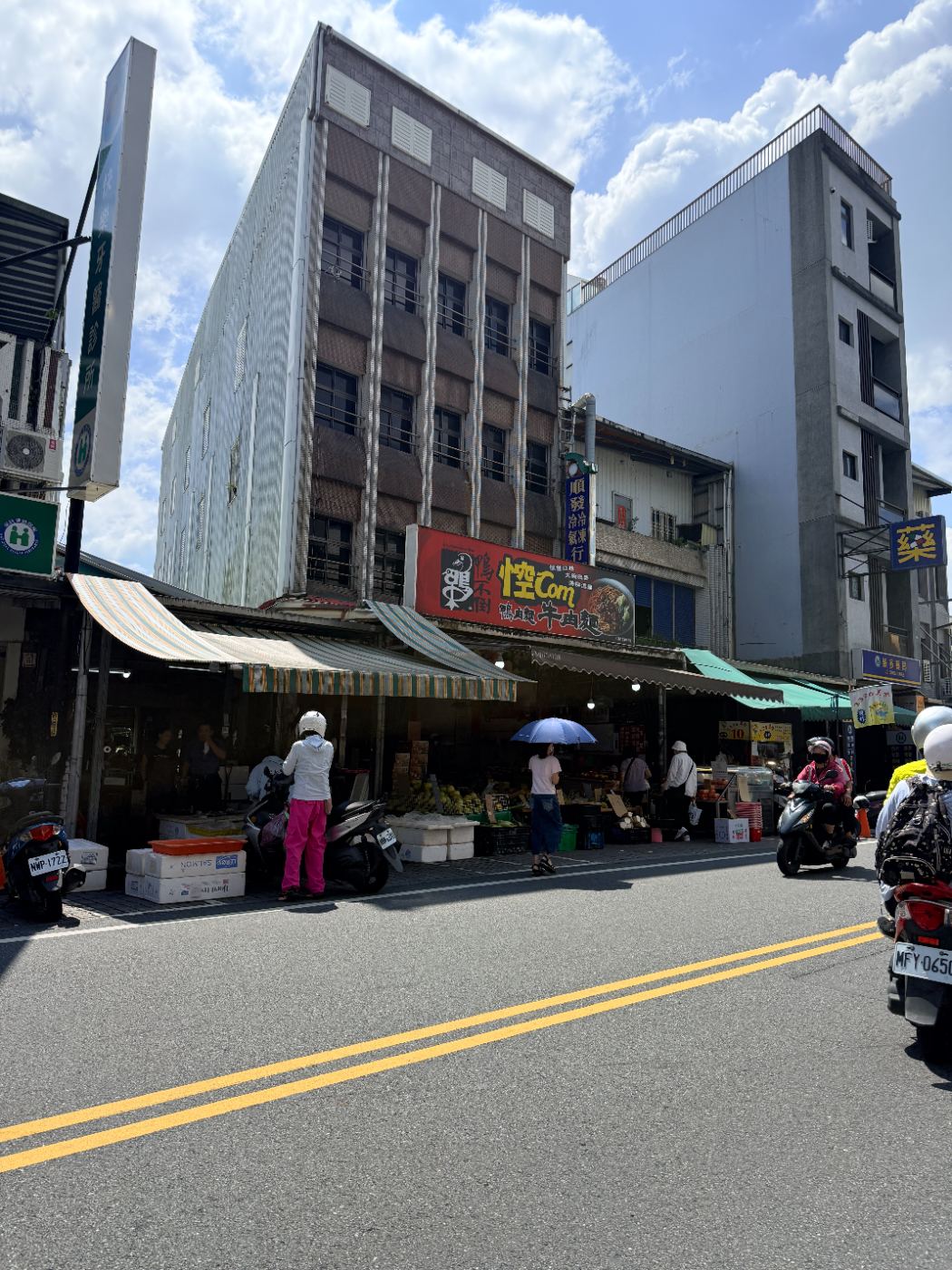 豔陽下人們在礁溪街道旁的傳統市場前行走和停放機車，市場入口與招牌清楚可見
