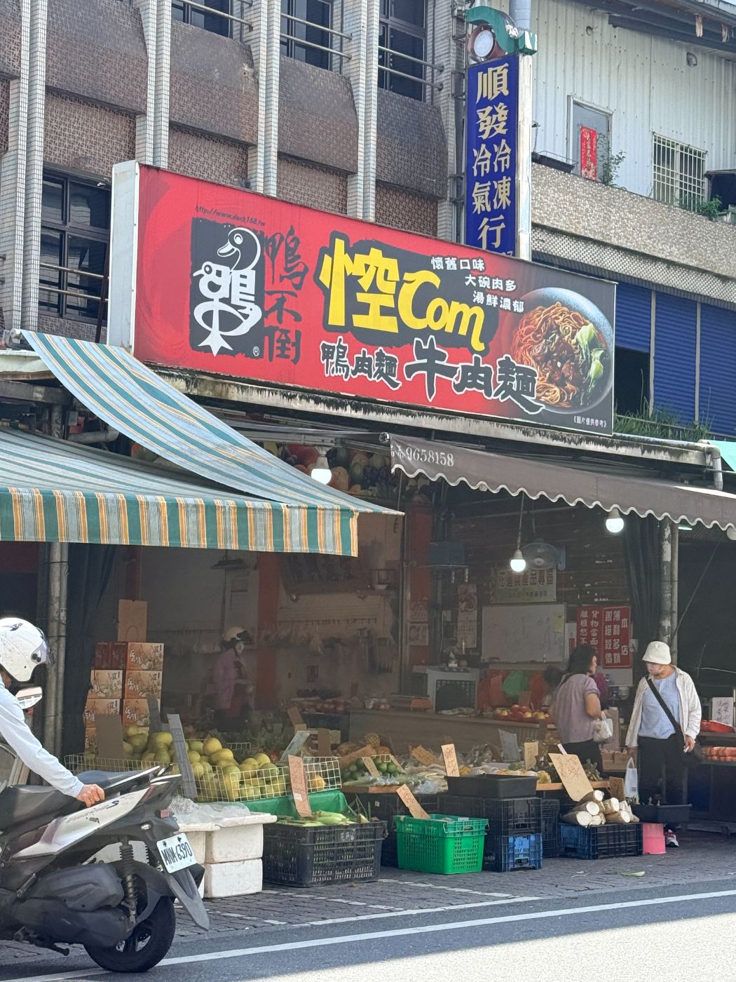 礁溪街道旁的傳統市場入口，招牌上有食品廣告，停有機車和有行人逛街